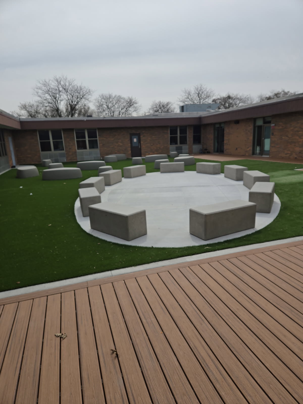 Outdoor courtyard at Bensenville Blackhawk School with circular concrete bench seating on artificial turf and composite wood deck flooring