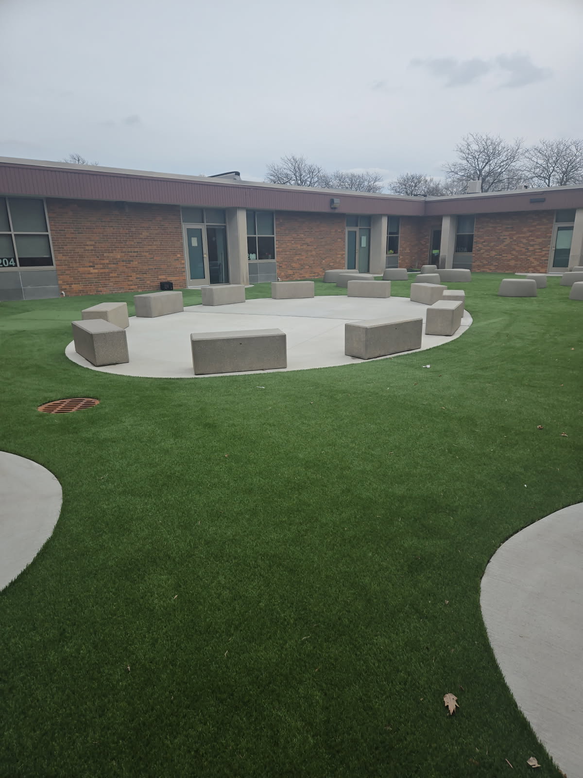 Concrete bench seating installation at Bensenville Blackhawk School featuring a circular concrete pad set in synthetic turf, providing a functional and modern outdoor gathering space.